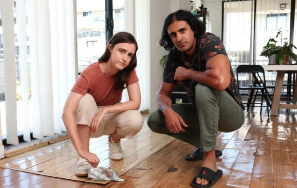 Photo of Faizan and Emma in their home showing damage to the floor. Photo by Tim Hunter