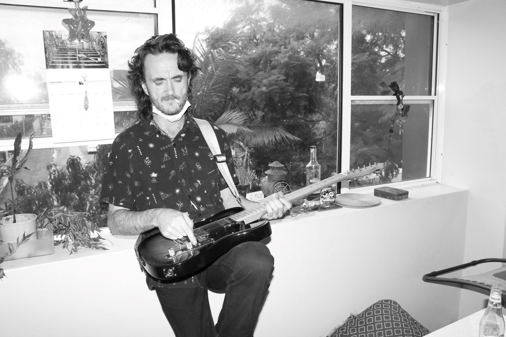 Black and white photograph of a man playing the guitar in front of a window